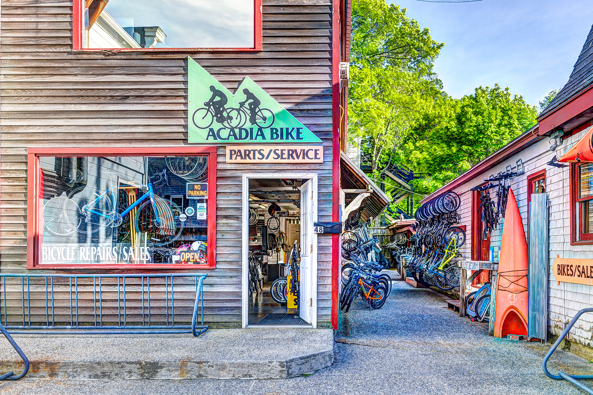 A storefront with a green sign reading 'Acadia Bike Parts/Service' and bicycles visible in the window and outside.