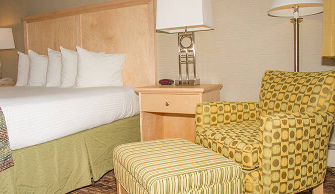 A hotel room with a bed, chair, lamp, and nightstand.