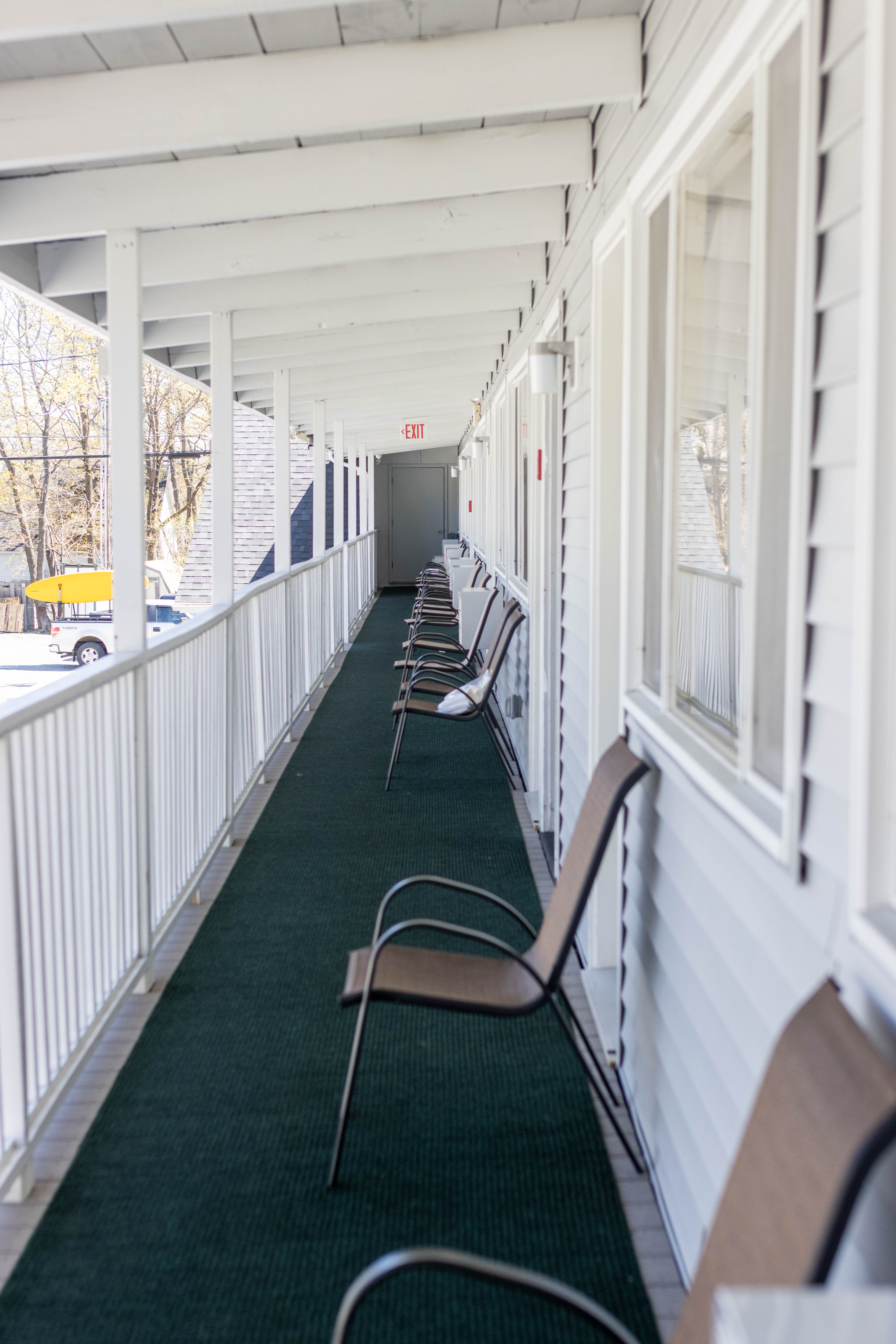 A long, covered hallway with green carpet and white siding, lined with chairs.