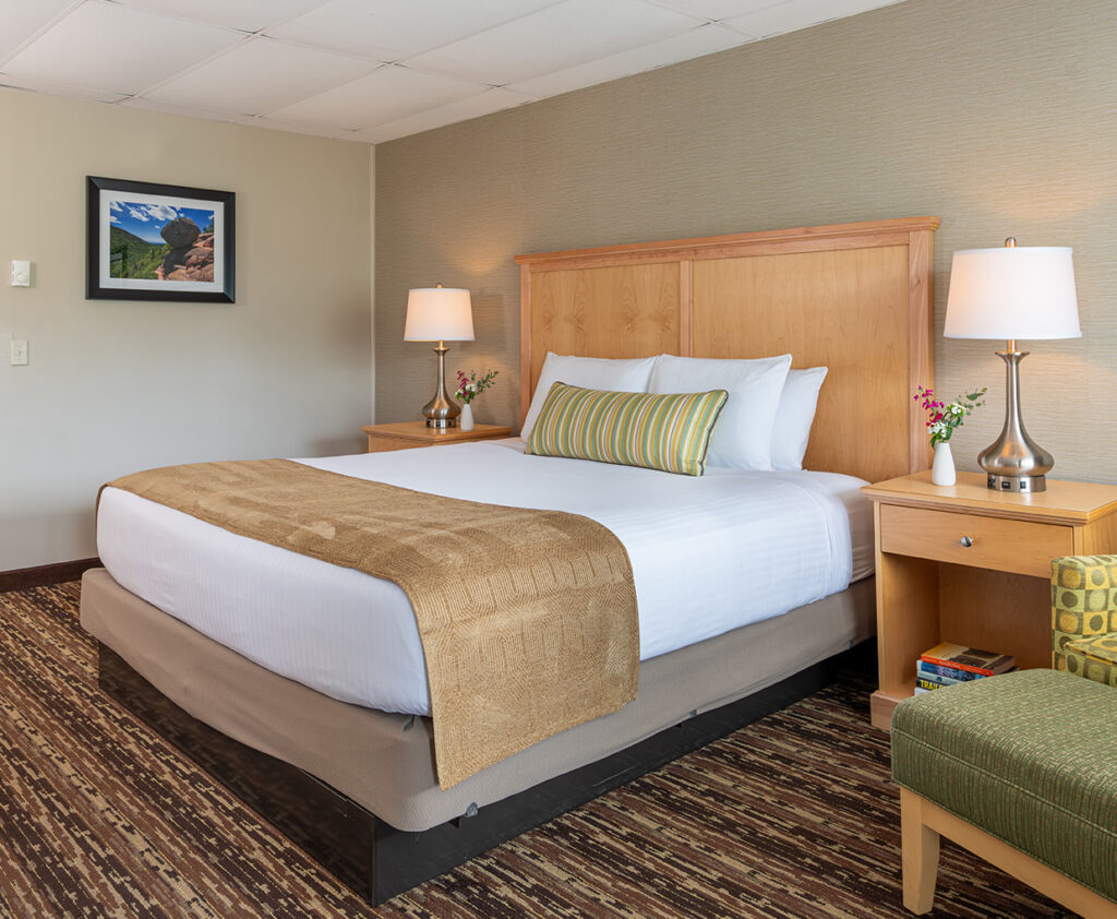 A neatly made hotel room with a large bed, two nightstands with lamps, and a chair.