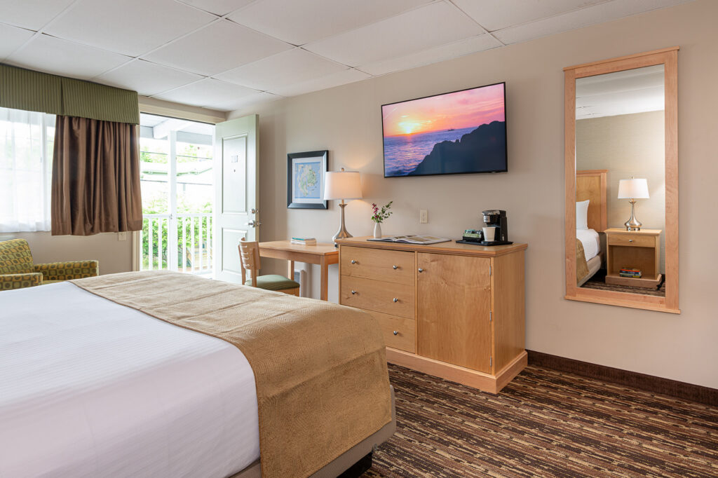 A hotel room with a bed, TV, mirror, desk, and dresser.