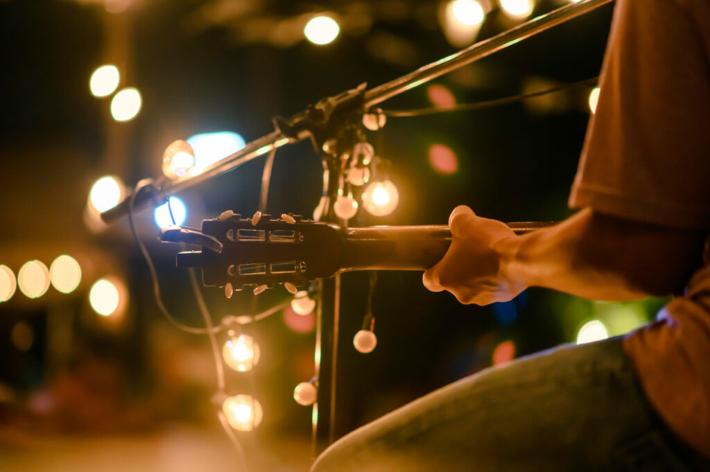 Musician playing guitar under string lights during a live music performance